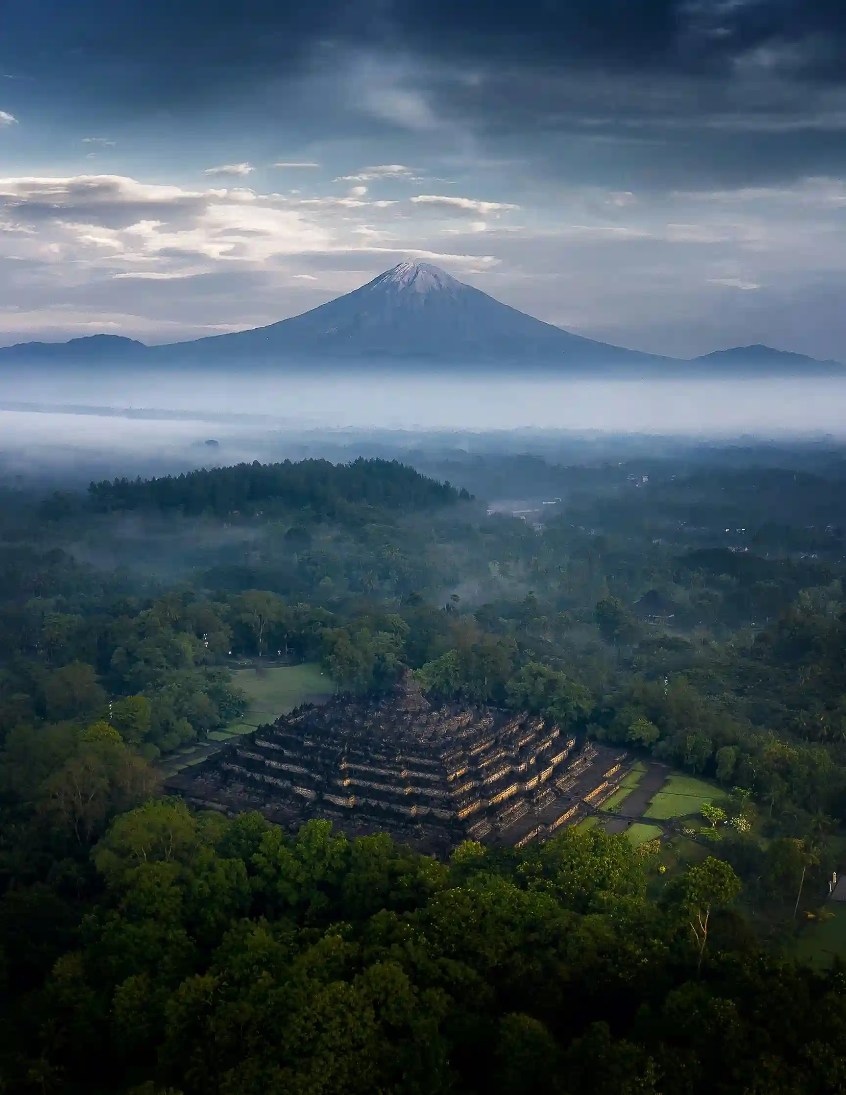 Borobudur Temple with misty jungle and volcano backdrop, a UNESCO highlight featured by icanfly in Indonesia cultural tours.