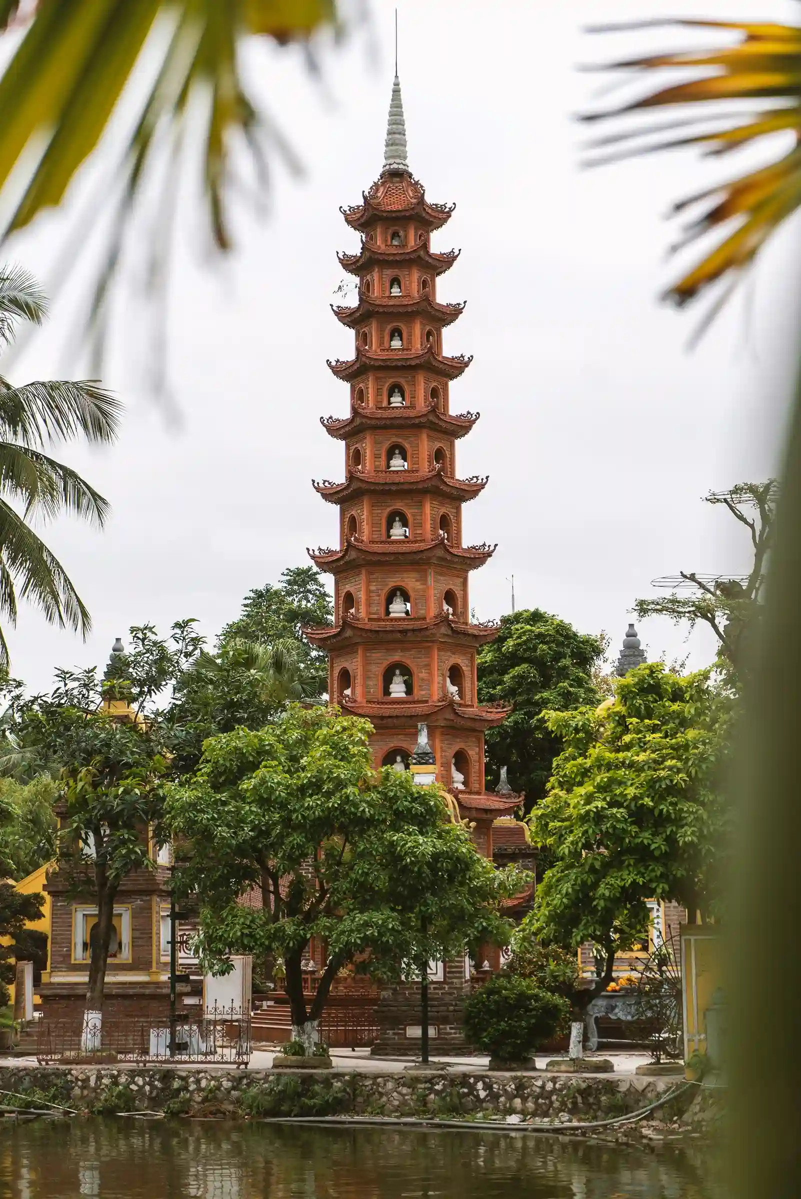 View of Tran Quoc Pagoda surrounded by trees in Hanoi, Vietnam, showcasing the city's rich heritage, ancient temples, and street life, promoted by icanfly.