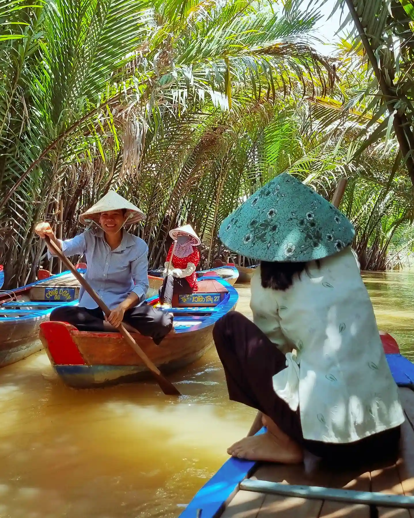 Locals paddling boats through palm-lined canals in Vietnam’s Mekong Delta, showcasing floating markets and rural life, highlighted by icanfly as a must-experience cultural journey.