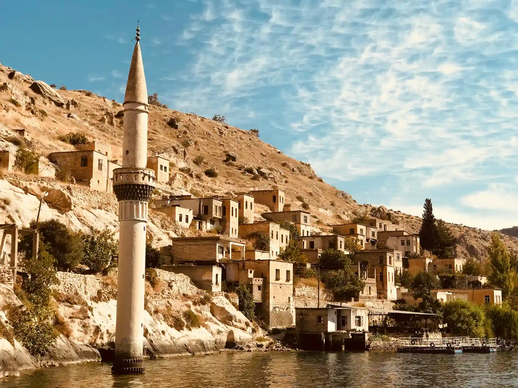 Scenic riverside village in Turkey with ancient architecture and a tall minaret, featured in icanfly's top travel escapes.